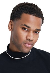 Pull à col roulé noir avec un collier de perles, mettant en valeur la texture lisse du tissu et un gros plan du visage avec des cheveux courts et bouclés.
