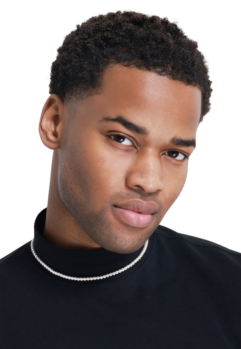 Pull à col roulé noir avec un collier de perles, mettant en valeur la texture lisse du tissu et un gros plan du visage avec des cheveux courts et bouclés.