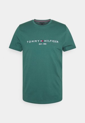 Groene katoenen t-shirt met ronde hals, met het witte logo "TOMMY HILFIGER" en de tekst "EST. 1985" gecentreerd op de voorkant. Korte mouwen, minimalistisch design.