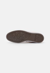 Suela de zapato de goma marrón con patrón de diamante para agarre, paredes laterales blancas y textura suave. Presenta un logotipo de marca cerca del talón.