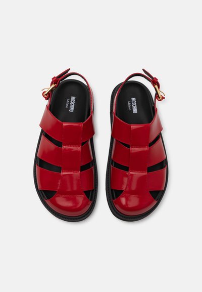 Punaiset patenttiliimasaappaat, joissa on avoin hihnadesign, mustalla pohjalla ja kullalla varustetulla soljella säätöä varten.