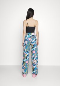 Pestrobarevné, vzorované kalhoty s širokým střihem na modrém podkladu, se růžovými akcenty a motivy blesků, spárované s černým, přiléhavým topem bez rukávů.