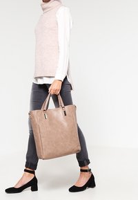 Bolso tote beige hecho de cuero sintético texturizado con dos asas. El bolso presenta acentos metálicos y un diseño minimalista.