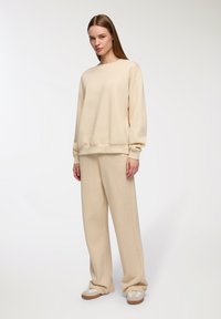 Kremowy sweter i pasujące spodnie z szerokimi nogawkami. Miękka tkanina, luźny krój, ściagacze przy rękawach i u dołu. Casualowe obuwie dopełnia cały strój.