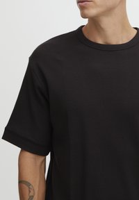 Sort ribbet t-shirt med rund hals, korte ærmer og en afslappet pasform. Stoffet har et struktureret mønster.