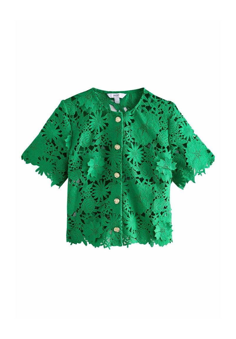 Veste courte à manches courtes en dentelle verte présentant des motifs floraux découpés, un col rond et des boutons dorés à l'avant. Longueur cropped.