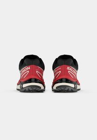 Rote und schwarze Trailrunningschuhe mit einer Gore-Tex-Schicht, die ein gewölbtes Design, eine strukturierte Sohle und sichtbare Logoakzente an der Ferse aufweisen.