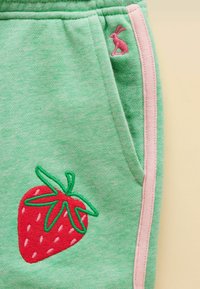 Roheline kangas roosa küljesõmmega, tikitud punane maasikas roheliste lehtedega ja väike roosa jänes tasku serva lähedal.