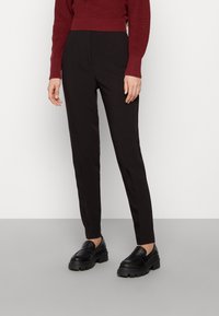 Black tailored pants made of smooth fabric, featuring a slim fit and a high waist, paired with chunky black loafers. Red knit sweater above.
