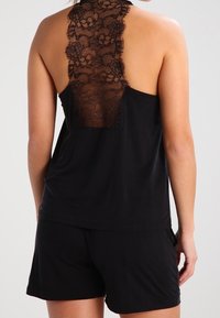 Top nero senza maniche con un design posteriore in pizzo floreale, abbinato a pantaloni corti neri. Tessuto morbido con una vestibilità rilassata e un leggero luccichio.