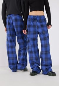 Blå rutig byxor med lös passform, med dragsko i midjan och svarta detaljer. De har en slät textur och bred bendesign.