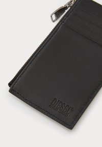 Čierna kožená peňaženka s textúrovaným povrchom, s uzáverom na zips a slotmi na karty na jednej strane. Logo Diesel je debossované v dolnom rohu.
