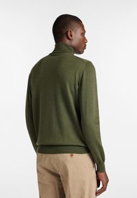 Maglione a maglia verde con colletto alto, maniche aderenti e orlo inferiore a coste. Texture liscia e design minimalista.