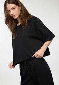 Maglietta nera oversize con maniche corte, realizzata in tessuto morbido. Presenta una vestibilità comoda e un orlo arrotondato, abbinata a pantaloni neri coordinati.
