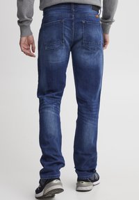 Menns mørkeblå denimjeans med rett snitt, fem lommer og subtil falming. Håndleddet har en svart etikett og sømdetaljer.