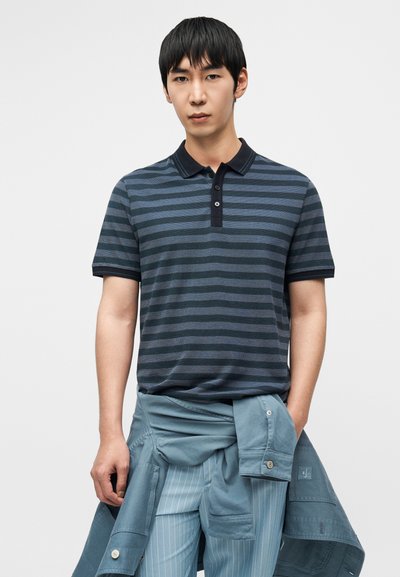 Μπλε-σκούρο ριγέ πόλο μπλουζάκι με κοντά μανίκια, μαύρο γιακά και πατιλέτα με τρία κουμπιά. Ανοιχτό μπλε παντελόνι με δεμένο σακάκι.