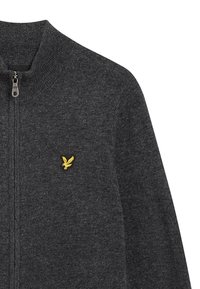 Donkergrijze zip-up sweater van gebreide stof, met een hoge kraag en een klein gele adelaarlogo op de linkerborst.