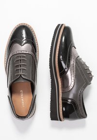 Chaussures brogues grises et noires avec une finition brillante, des accents texturés, des perforations décoratives et une semelle robuste à détails superposés.