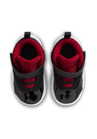 Czarne lakierowane buty z czerwonymi akcentami z siateczki, fabriczną wszywką i rzepem. Posiadają białe podeszwy oraz zaokrąglony kształt.