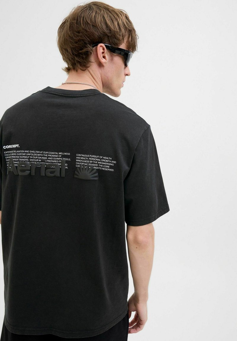 Sort bomulds t-shirt med korte ærmer, der har et stiliseret grafisk design og tekst på bagsiden i hvid. Rund hals og afslappet pasform.