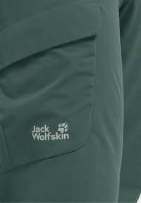 Poche en tissu vert avec rabat portant le logo blanc "Jack Wolfskin" et une empreinte de patte sur un vêtement d'extérieur.