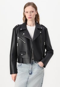 Svart kunstskinnet cropped bikerjakke med sølvglidelåser, spiss krage og trykknappdetaljer. Kombinert med et lyseblått denimminiskjørt.