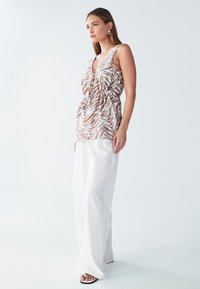 Brun- og hvide mønstrede ærmeløse top med indsnøret talje, kombineret med løse hvide bukser og sorte og hvide sandaler med åben tå.