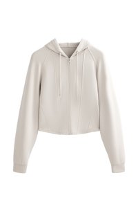 Felpa corta beige chiaro con zip frontale, cappuccio con cordino e polsini a costine. Tessuto liscio con dettagli delle cuciture.