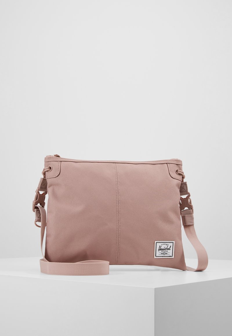 Borsa a tracolla rosa in tela con una texture liscia, dotata di chiusura a zip, tracolla regolabile e un'etichetta bianca del brand sul fronte.