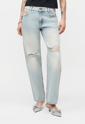 Jeans strappati a lavaggio chiaro con gambe dritte indossati con décolleté argento a punta con tacco kitten e una maglietta nera.