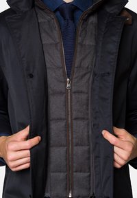 Granatowa kurtka zewnętrzna z zapinaną na zamek szarą kamizelką wewnętrzną. Brązowe akcenty z przodu. Teksturowany materiał z wyściełanym wzorem w warstwie wewnętrznej.