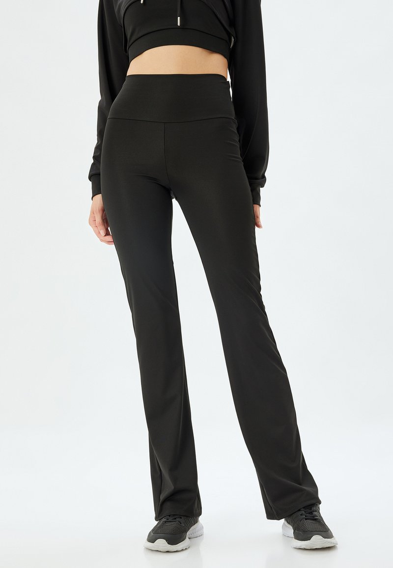 Zwarte sportleggingen met een hoge tailleband, een gladde textuur en een aansluitende pasvorm. Draagt een cropped zwart topje en donkere sneakers.