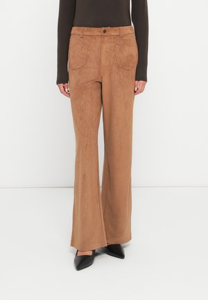 Pantaloni flared in suede marrone con due tasche posteriori e cuciture a vista. Indossati con un top aderente a maniche lunghe e décolleté neri a punta.