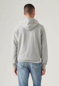Grijze hoodie van een katoenmix, met een trekkoordcapuchon, lange mouwen en geribde manchetten. Draagt met lichtblauwe jeans.