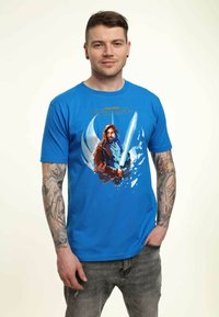 Camiseta de algodón azul con un gráfico de un personaje con un sable de luz, rodeado de un diseño circular. Mangas cortas y cuello redondo.