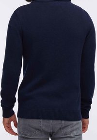 Pull en maille bleu marine avec un col montant, des poignets et un ourlet côtelés. Présente un motif texturé, porté par une personne vue de dos.