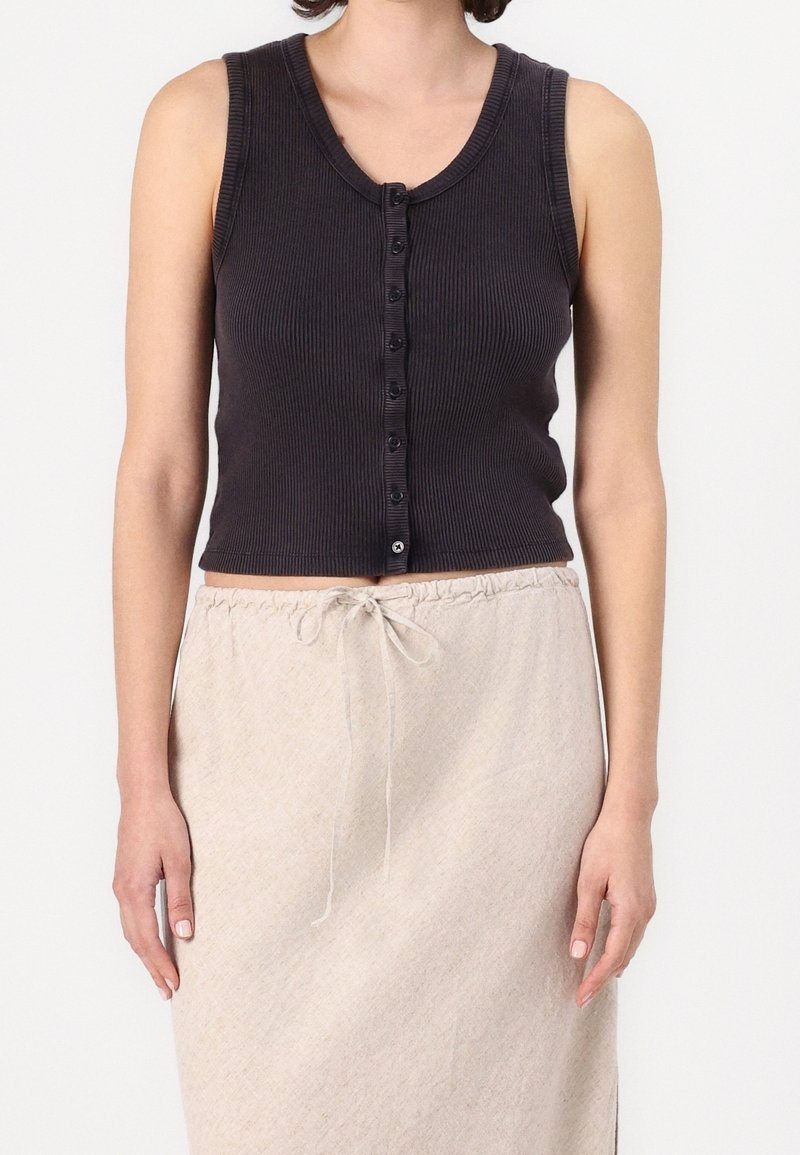 Svart ribbad linne med rund halsringning och knappstängning framtill. Bärs med en ljusbeige kjol med dragsnöre.