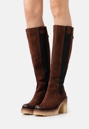Brown suede knee-high boots with a black elastic panel, a rounded toe, and a chunky clear heel. Features contrast stitching and accents.