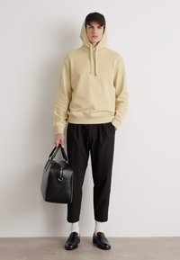 Felpa con cappuccio beige, pantaloni neri aderenti, borsa in pelle nera, calzini bianchi e mocassini neri. Design semplice, vestibilità moderna e colori neutri.