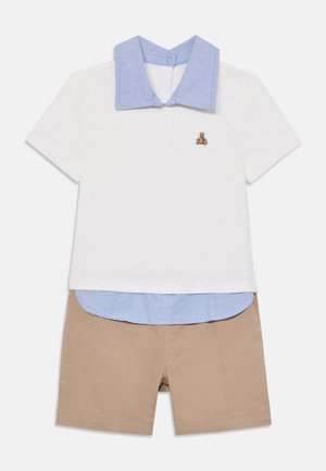 Korte mouw witte polo met een blauwe kraag, gelaagd over een lichtblauw shirt, gecombineerd met beige shorts. Bevat een kleine geborduurde afbeelding.