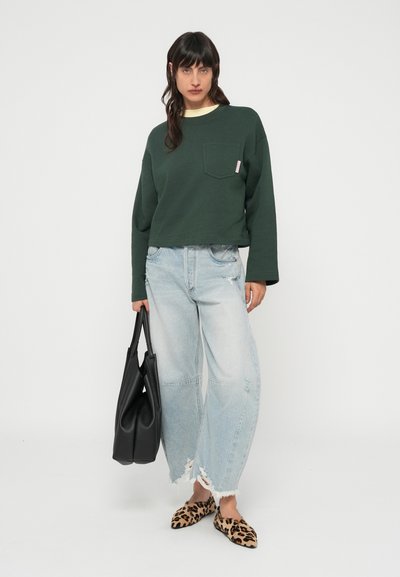 Σκούρο πράσινο cropped φούτερ με τσέπη, ανοιχτό μπλε τζιν με φθορές, μαύρη τσάντα και παντόφλες με λεοπάρ σχέδιο.