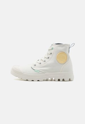 Bottines en toile blanche avec une semelle en caoutchouc texturée, un orteil renforcé et un logo circulaire jaune sur le côté. Comprend des accents bleu clair.