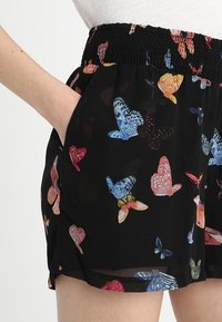 Svarta shorts med färgglada fjärilmönster, utrustade med rynkad midja och sidofickor. Tillverkade av lätt, texturerad tyg.