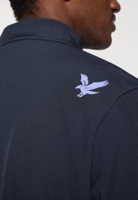 Jachetă navală cu un imprimeu violet deschis cu un vultur pe partea superioară a spatelui, realizată dintr-un material neted și ușor, cu un guler structurat.