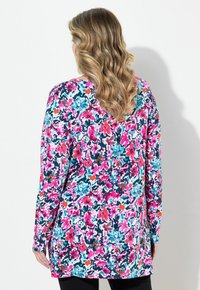 Tunica a maniche lunghe con un vivace motivo floreale, caratterizzata da fiori rosa, blu e arancione su uno sfondo bianco, con una vestibilità ampia e scollatura a girocollo.