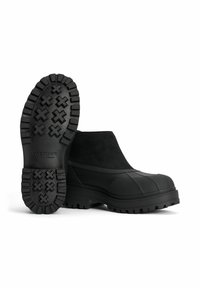 Svarta ankelstövlar med gummisula, överdel av mocka och ett strukturerat mönster på sulan. Har en slät yta och elastiska sidor för enkel påtagning.