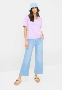 Lyse lilla kortærmet top med V-hals, parret med lyse denim brede bukser. Tilbehøret inkluderer en lyseblå bucket hat og mønstrede sandaler.