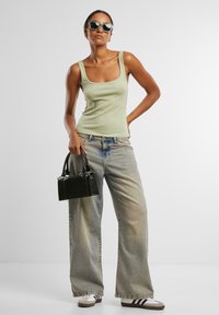 Kaki tanktop, oversized falmede denimbukser, sort håndtaske med metalaccenter og hvide sneakers med mørke striber. Klare solbriller.