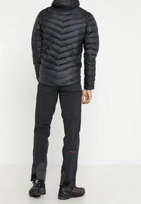 Černá nadýchaná bunda s vzorem šípů a kapucí, spárovaná s černými kalhotami. Kalhoty mají zipy na dolní části nohavic a červený akcent s logem.