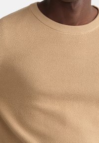 Pull en tricot beige avec un motif texturé, un col côtelé et une coupe décontractée en tissu doux et léger.